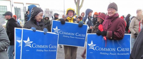 three people at a protest holding blue signs that say "Common Cause Oregon"
