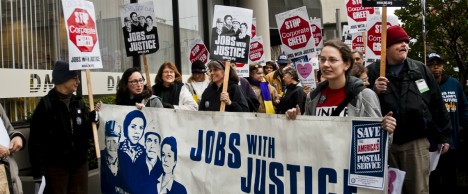 A group of people protesting and holding a large banner reading "Jobs with Justice"
